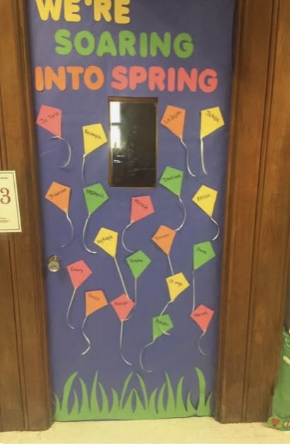 Soaring into spring classroom door with colorful kites labeled with student names on a blue sky background.