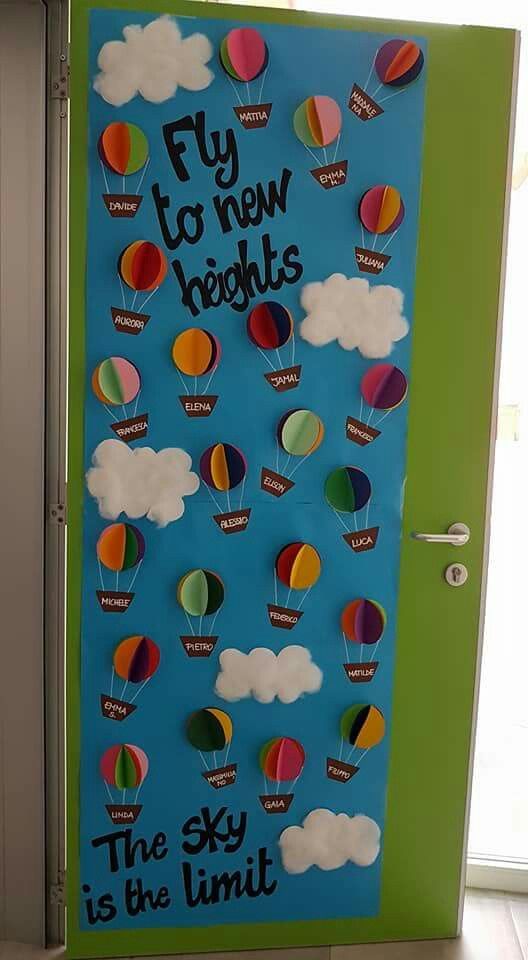 Hot air balloon-themed classroom door with student names on 3D balloons floating in a blue sky.