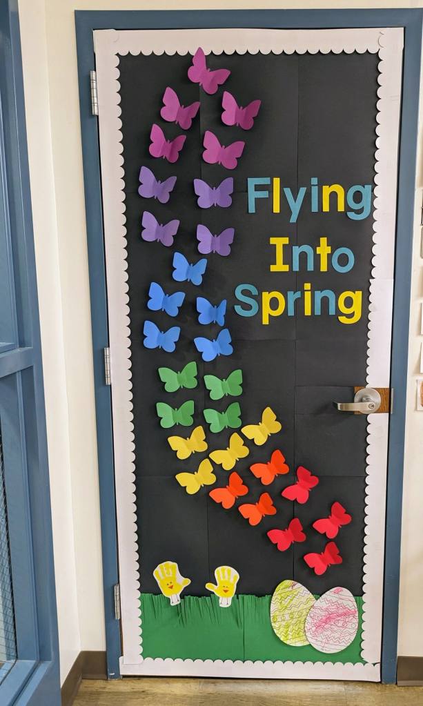 Butterfly-themed spring classroom door with a rainbow gradient of paper butterflies flying upward.
