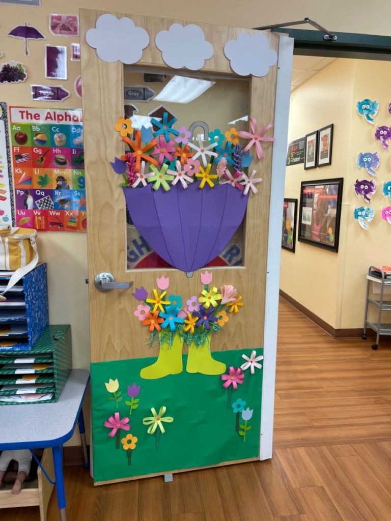 Spring rain boot classroom door featuring an umbrella overflowing with flowers and clouds above.