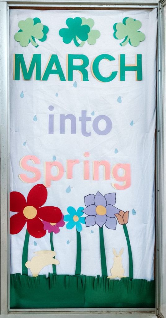 March-themed classroom door with shamrocks, raindrops, and blooming spring flowers.
