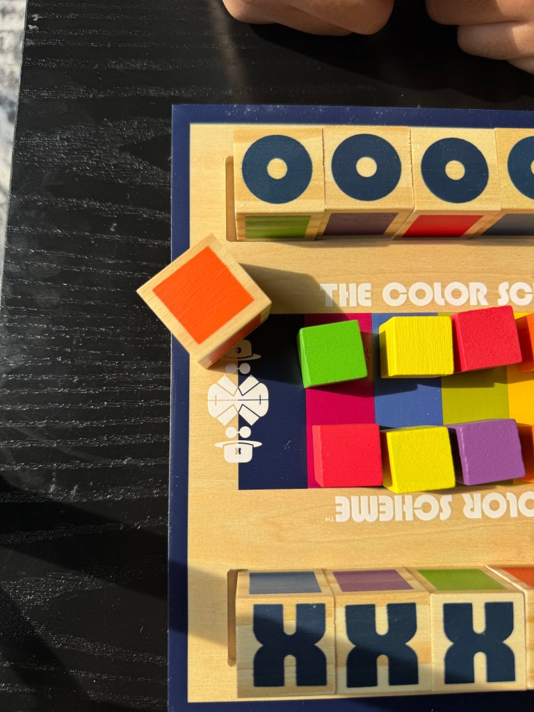 Close-up view of 'The Color Scheme' board game showing colorful blocks and code cubes on a wooden game board.