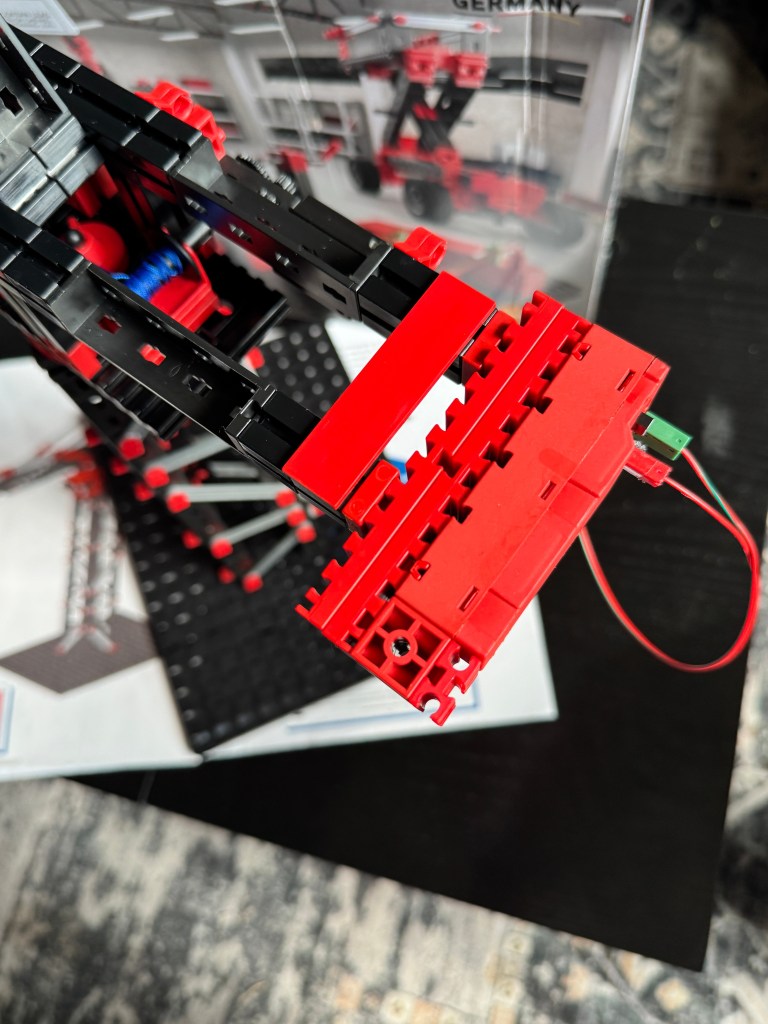 Close-up of a red and black Fischer Technik building kit, showcasing intricate parts and wiring, with a manual and base plate visible in the background.