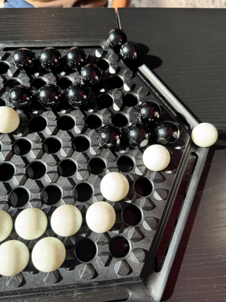 Close-up of an Abalone game board featuring black and white marbles positioned on a hexagonal grid.