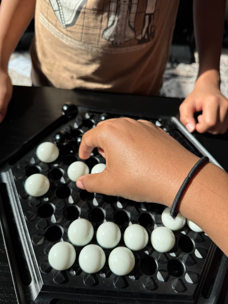 A hand reaching for a white marble on a hexagonal board game, with black marbles visible in the background.