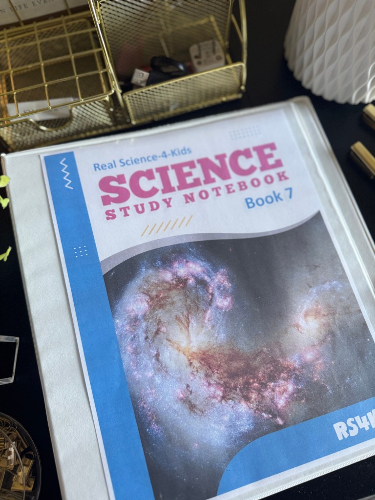 A close-up of the cover of 'Real Science-4-Kids Book 7 Study Notebook' featuring a colorful design and an image of a galaxy.