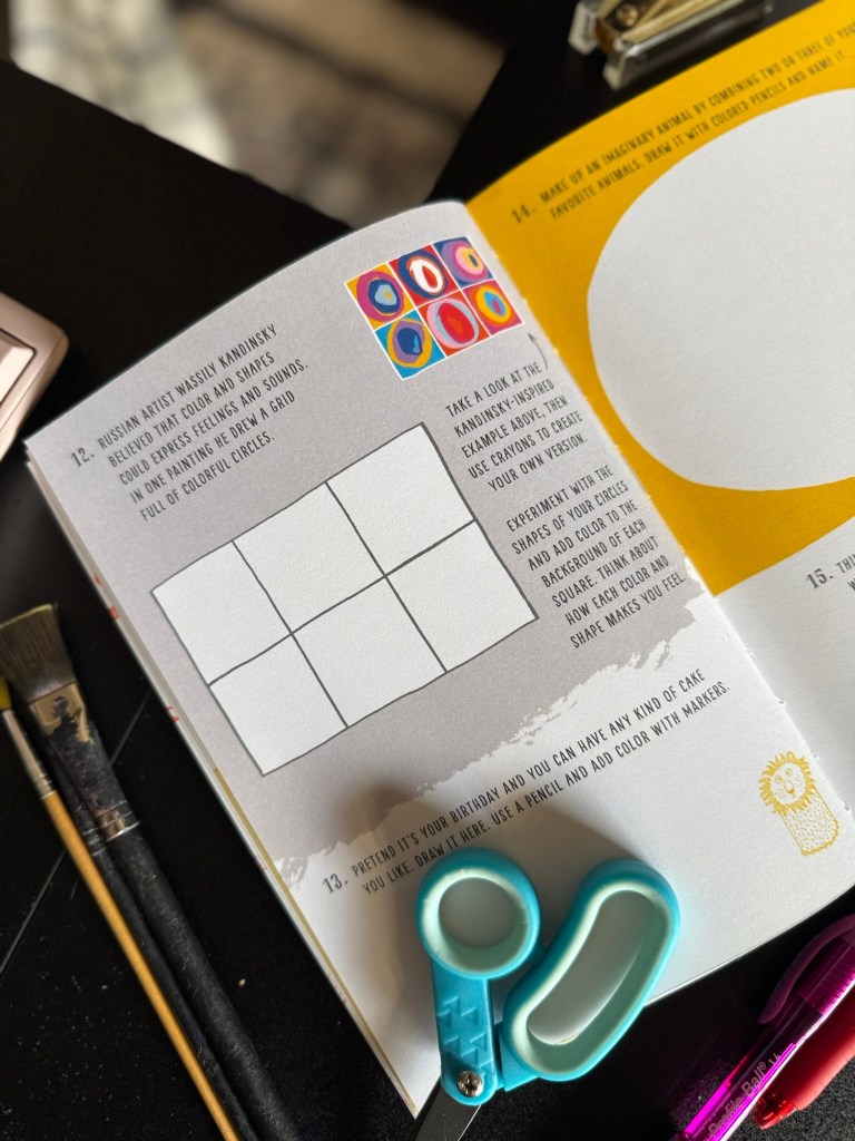 An open art book featuring creative prompts, with colorful examples inspired by artist Wassily Kandinsky, alongside scissors and paintbrushes on a black table.