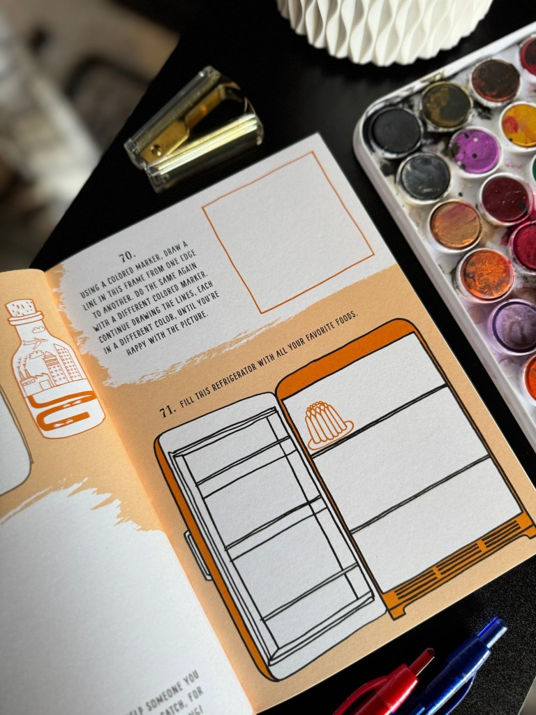 An art prompt page from the book 'My Year of Art,' featuring instructions to draw and fill in a refrigerator with favorite foods, along with a colorful paint palette and pens nearby.
