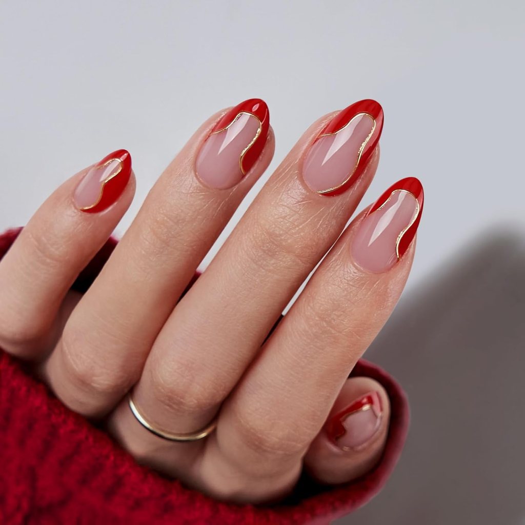 Close-up of a hand with manicured nails featuring a red and nude design with gold accents.