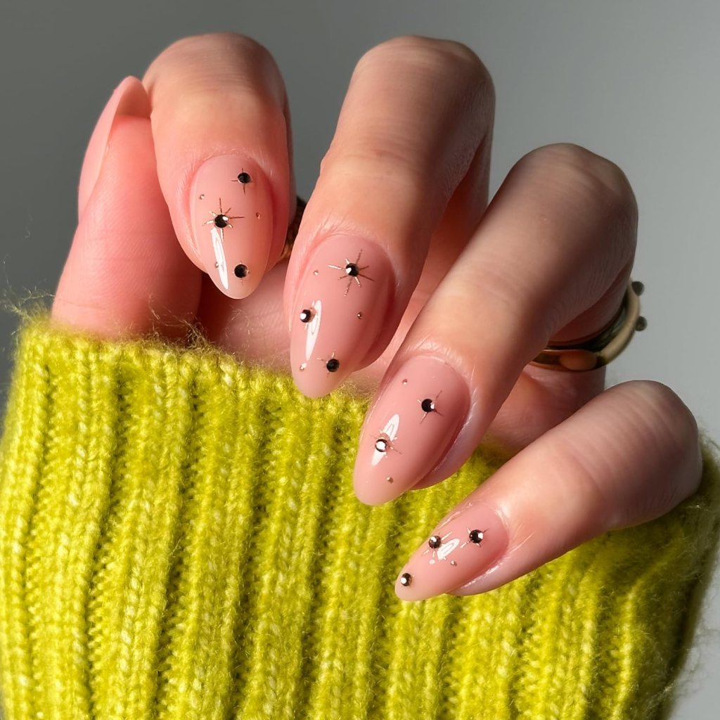 Close-up of a hand with well-manicured nude nail polish adorned with black and white nail art designs, resting on a bright green knitted sweater.