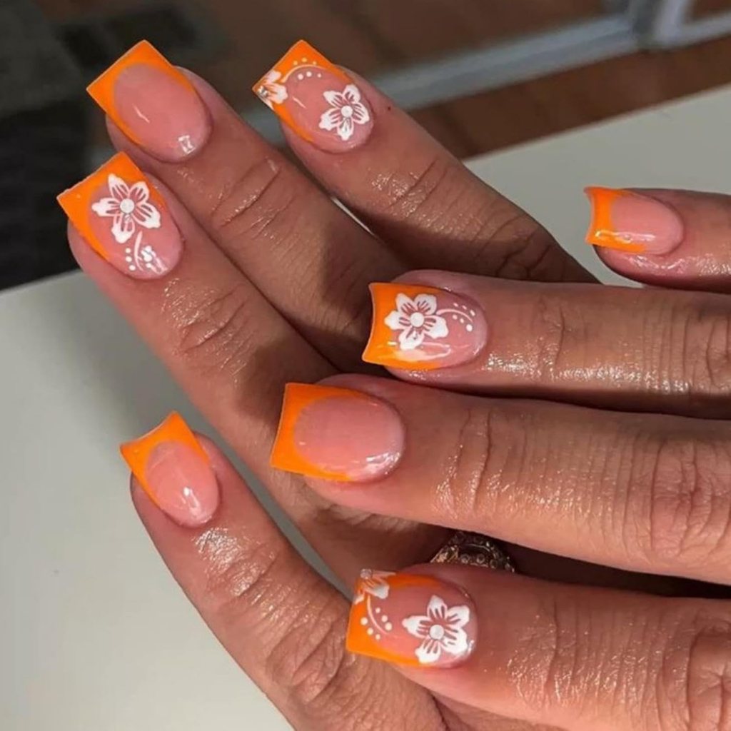 Nude nails with bright orange French tips and white floral nail art