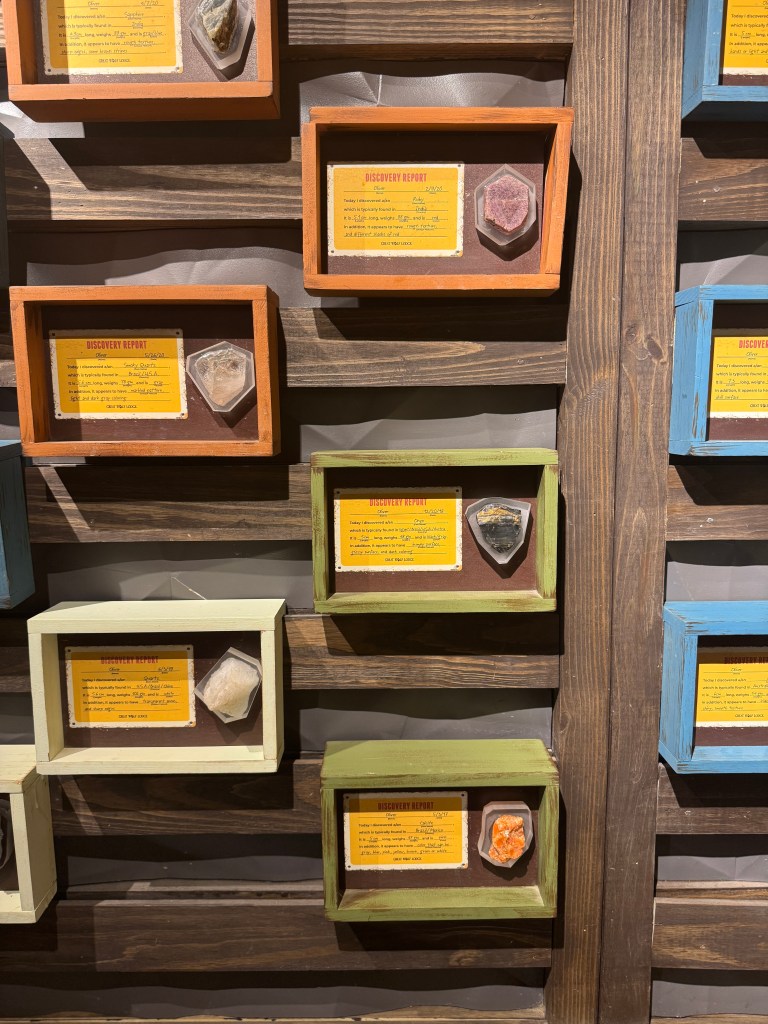 Close-up view of a display featuring various gemstones in colorful frames, each accompanied by descriptive labels detailing their properties and discovery information.