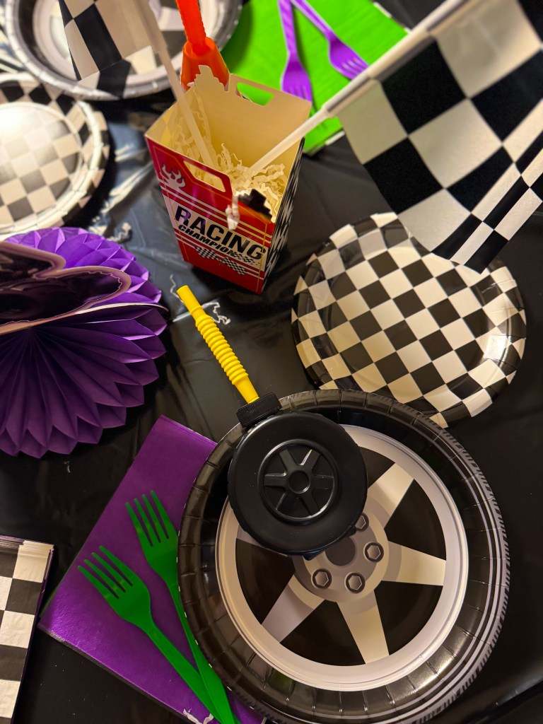 Monster truck birthday party table decor with tire themed plates, racing popcorn box, and colorful utensils on a Monster Jam party table.