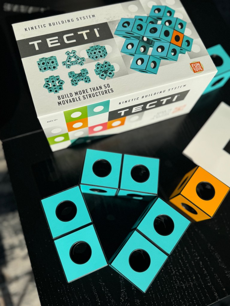 Box of the Tecti kinetic building system featuring turquoise and black cubes, with an orange cube beside it, showcasing instructions for building movable structures.