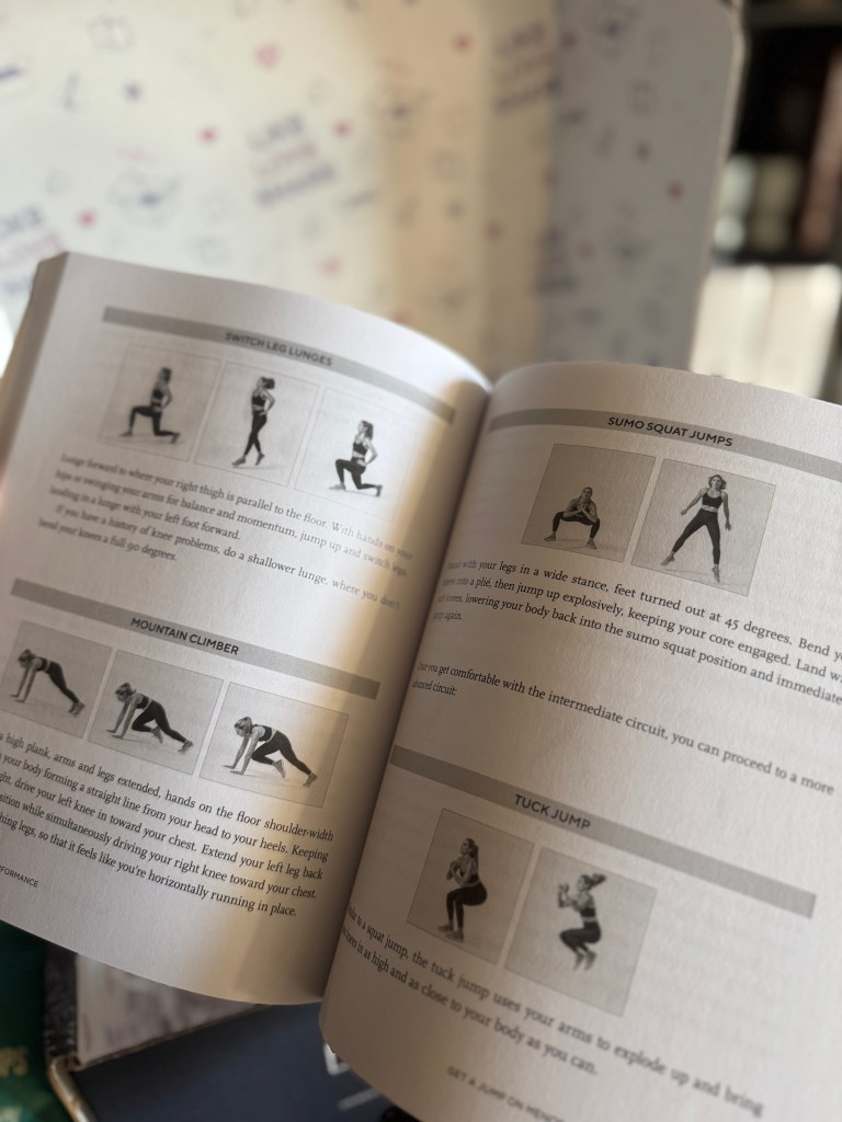 An open fitness book displaying exercises with images, including switch leg lunges, sumo squat jumps, mountain climbers, and tuck jumps. The background features a patterned surface.