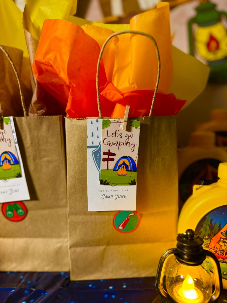 Camping party favor bag with “Let’s Go Camping” tag and orange and yellow tissue paper.