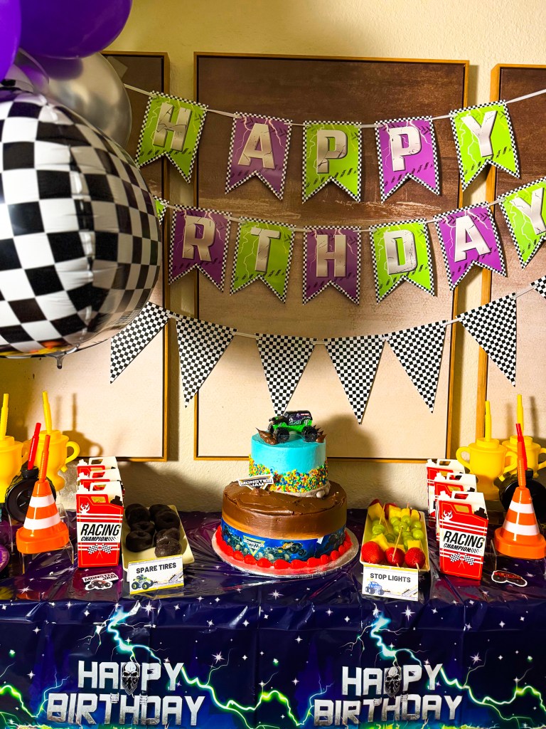 Monster truck birthday cake centerpiece on a Monster Jam themed party table with racing decorations and checkered flags.