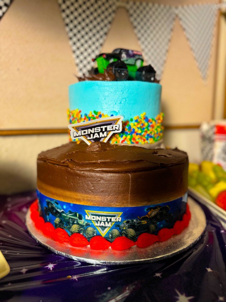 Monster Jam birthday cake with chocolate frosting and toy monster truck topper on a racing themed dessert table.