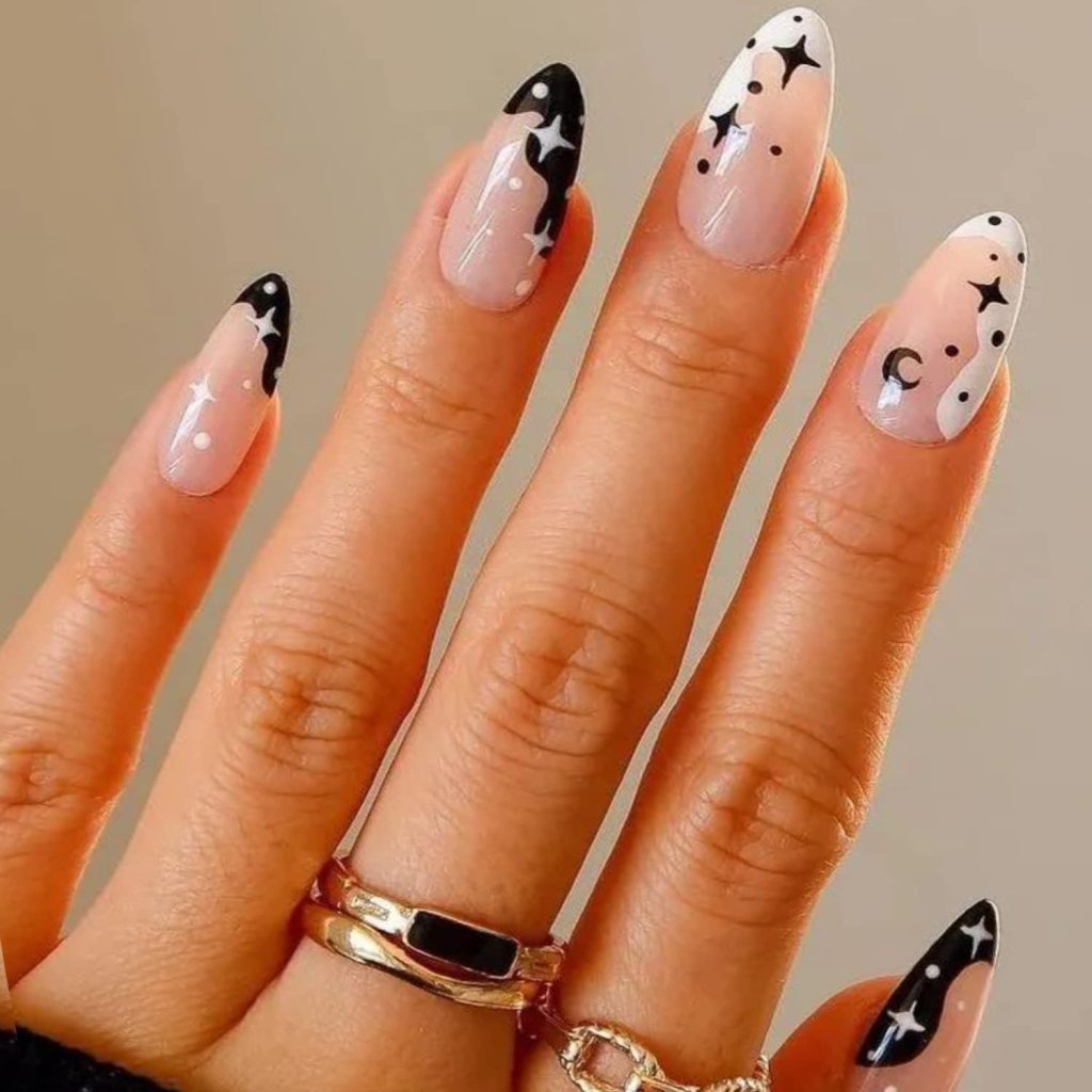 Close-up of manicured nails featuring a gradient from nude to clear with black tips, adorned with white stars and crescent moon designs.