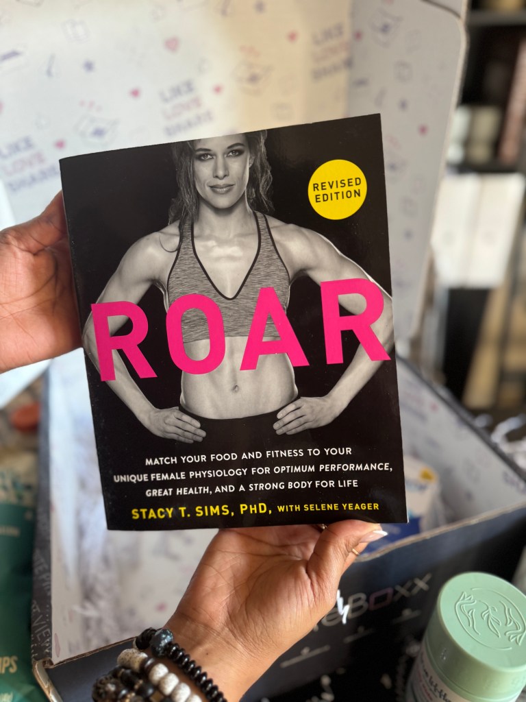A hand holding the book 'ROAR' by Stacy T. Sims, featuring a fit woman on the cover, highlighting its focus on female physiology and fitness.
