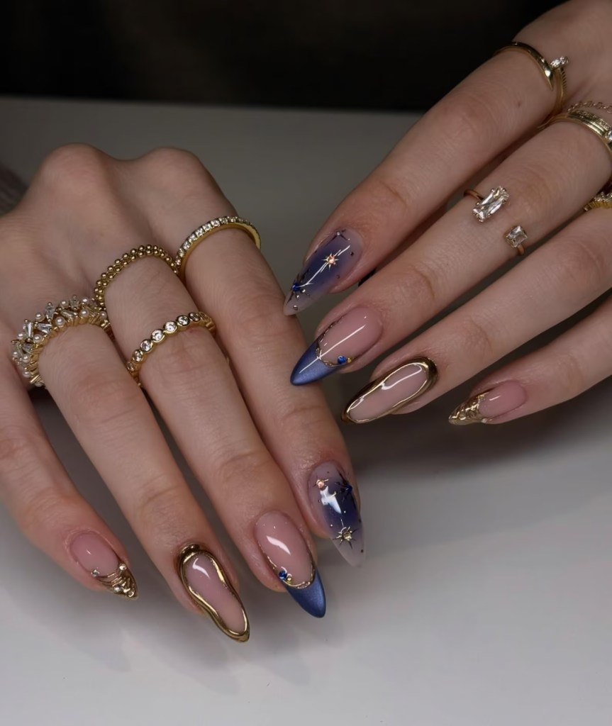 Navy blue chrome almond nails with gold metallic accents, celestial star details, and glossy nude polish.
