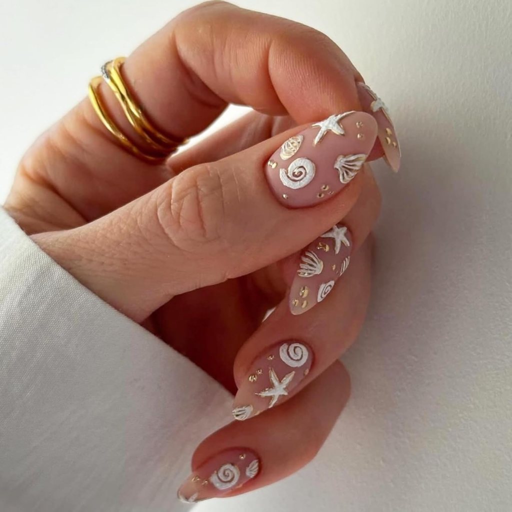 Minimalist seashell ocean nails with gold accents, nude pink polish, and classy beach-inspired nail art
