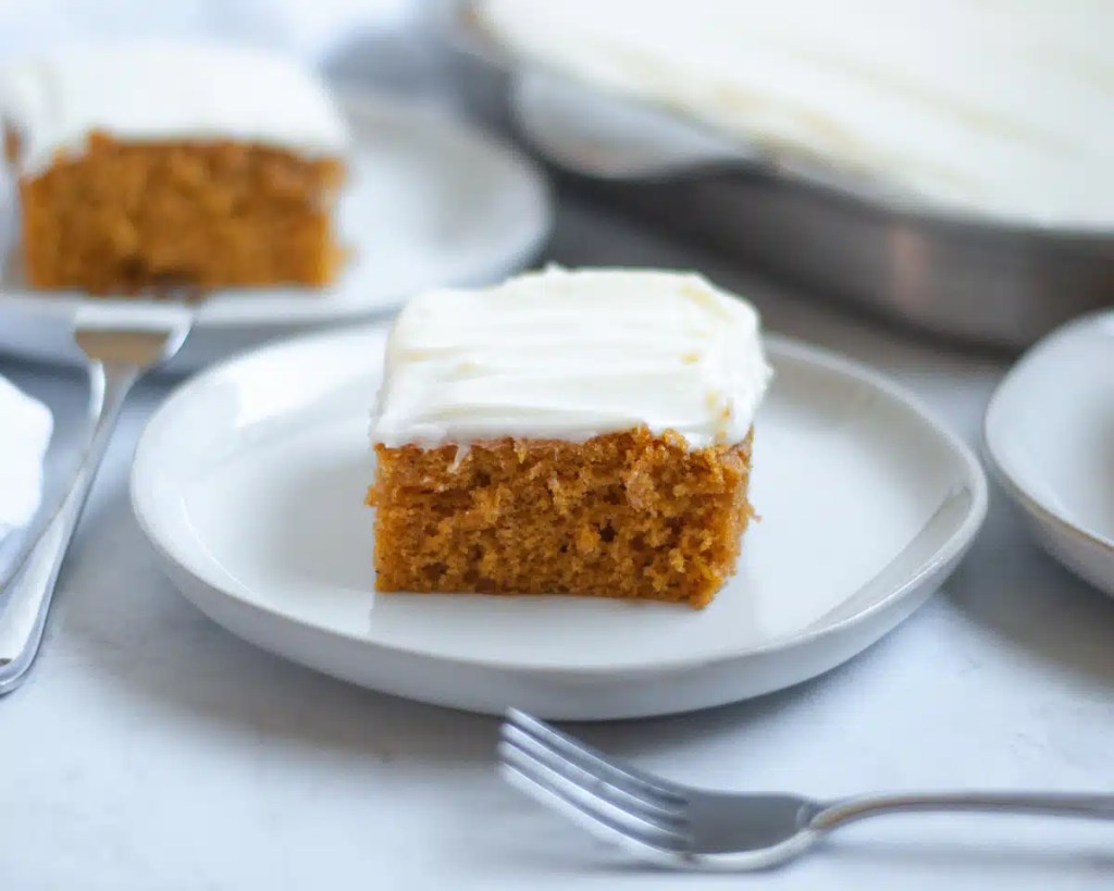 A slice of Pumpkin Bundt Cake with cream cheese frosting on a white plate, accompanied by a fork.