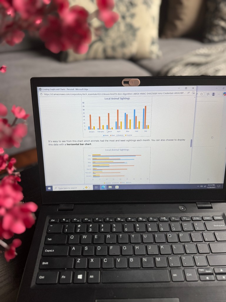 A laptop displaying a lesson about creating graphs and charts, featuring a horizontal bar chart titled 'Local Animal Sightings' with various colored bars for different months. In the background, a soft-focus floral decoration is visible.