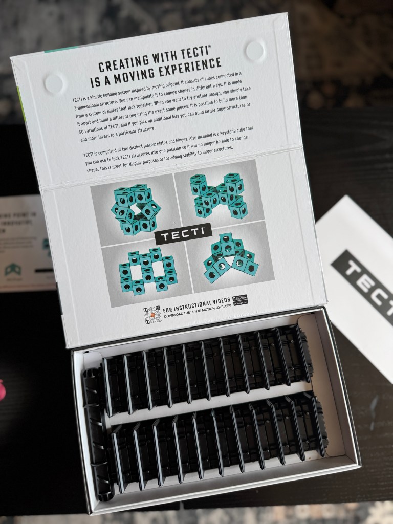 Open box of Tecti kinetic building system showcasing turquoise cubes and black connectors, with visual instructions for assembly.