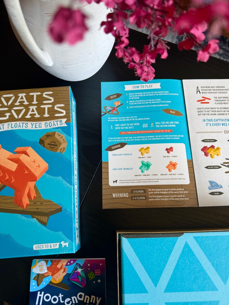 Board game 'Goats on Goats' box and instructions featuring gameplay steps, a description of winning conditions, and colorful graphics. A small card labeled 'Hootenanny' is also visible, along with a decorative vase and flowers in the background.