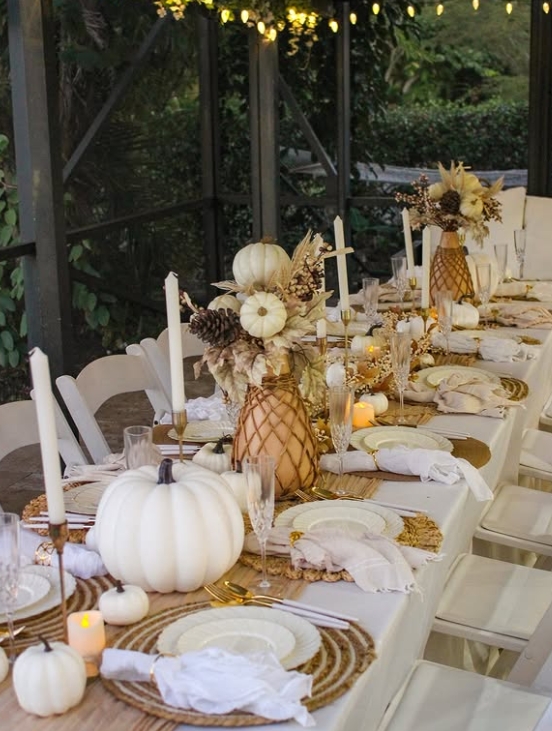 A beautifully styled Thanksgiving table featuring white pumpkins, elegant dinnerware, and natural textures, illuminated by soft candlelight.