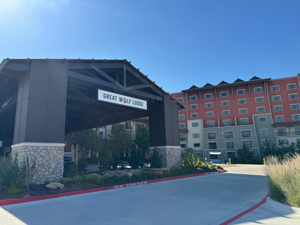 Exterior view of the Great Wolf Lodge entrance, showcasing the lodge's sign and surrounding landscaping under a clear blue sky.