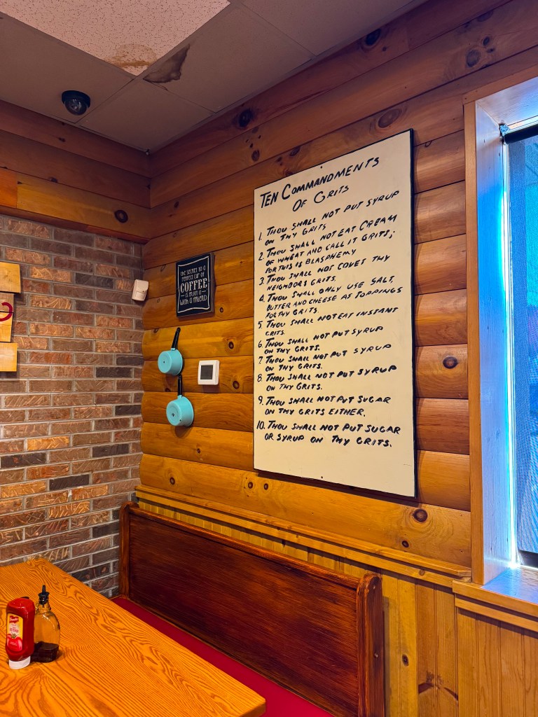 Southern-inspired Ten Commandments of Grits wall art hanging above a wooden restaurant booth at Flapjack's.