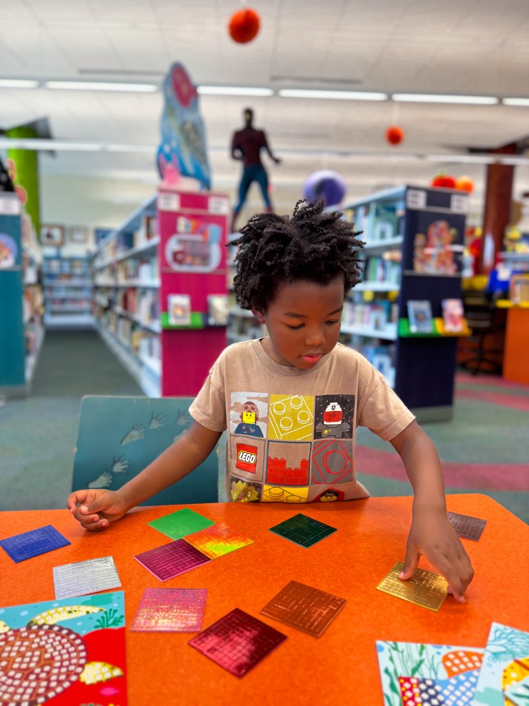 Child choosing metallic mosaic sticker sheets during a fine motor kindergarten activity.
