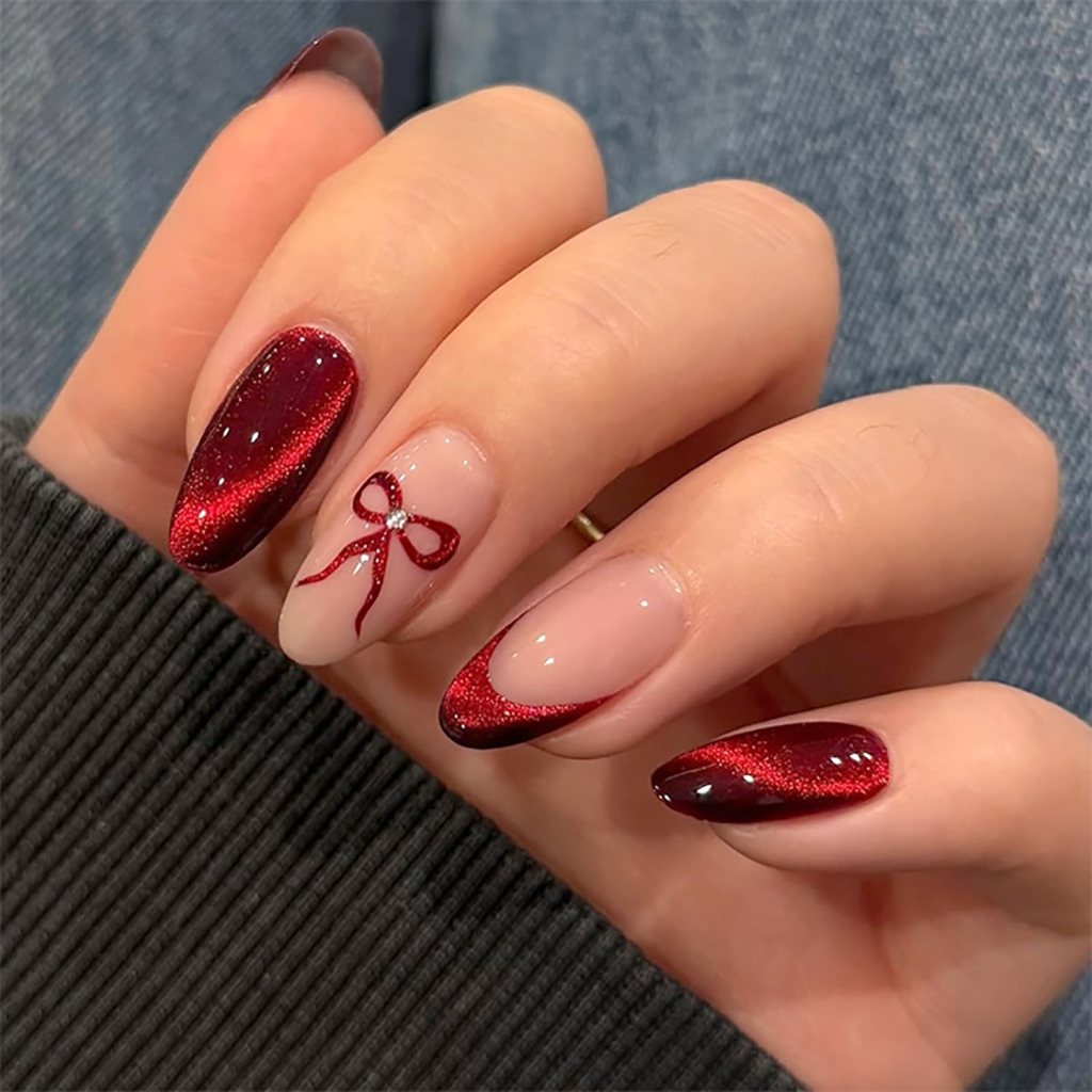Close-up of a hand showing stylish manicure with red glitter and a bow design on a nude nail.