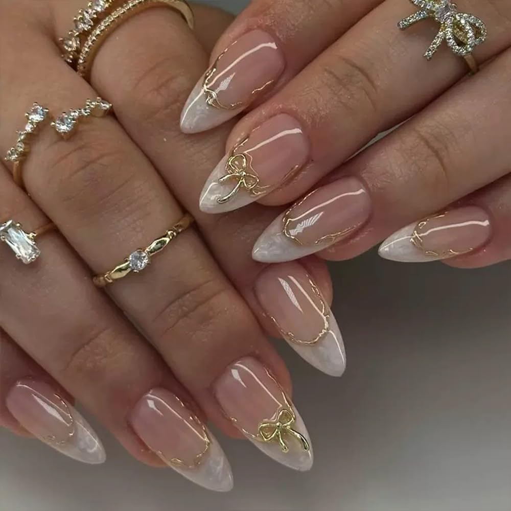 Close-up of hands with long, pointed nails featuring a nude base and white tips, adorned with gold accents and rings.