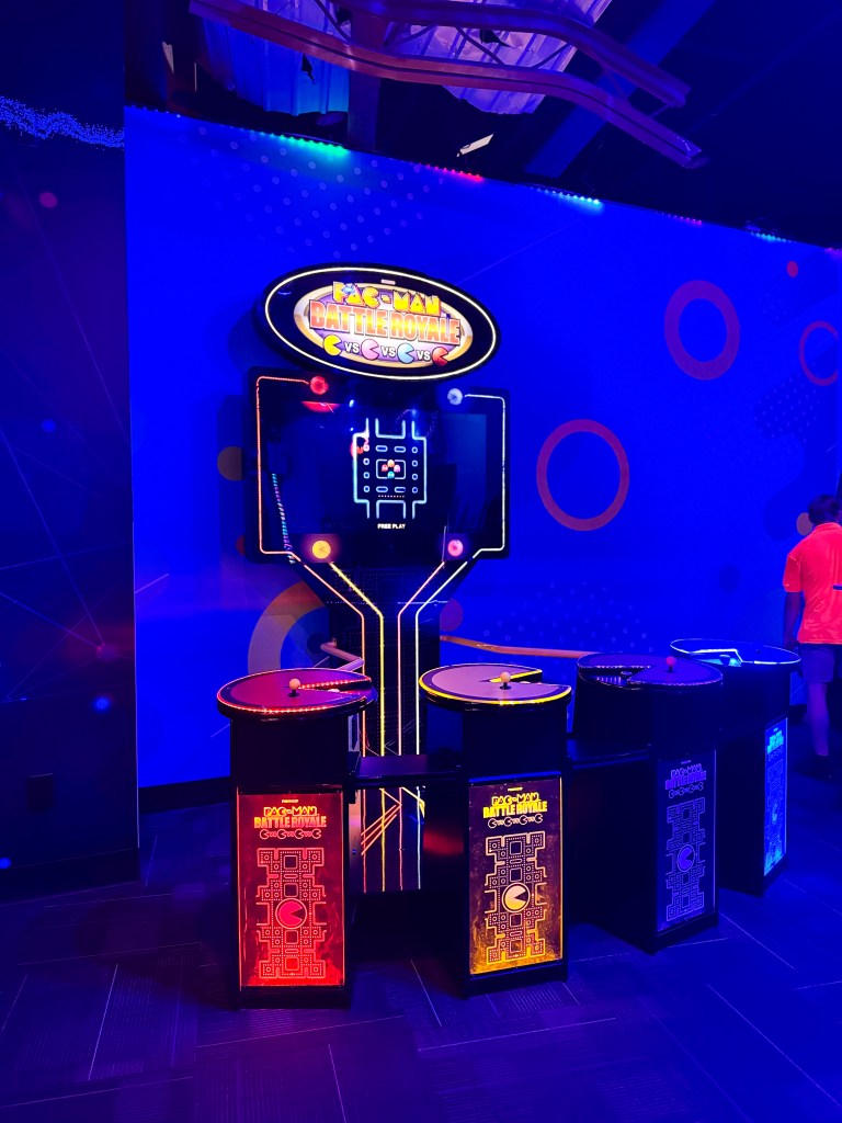Pac-Man Battle Royale arcade game with multi-colored control panels in a brightly lit room.