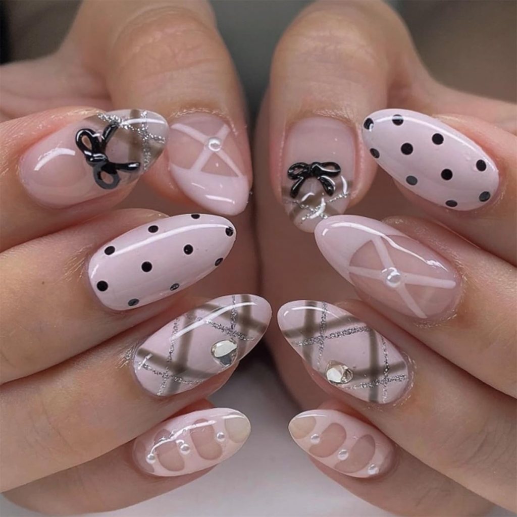 Close-up of manicured nails featuring a variety of designs, including pink polish with black polka dots, bows, and transparent geometric patterns embellished with crystals.