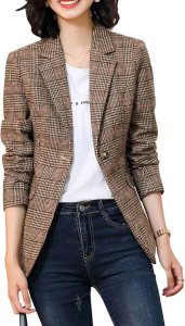 A person wearing a plaid blazer over a white t-shirt paired with dark jeans, smiling while standing against a neutral background.