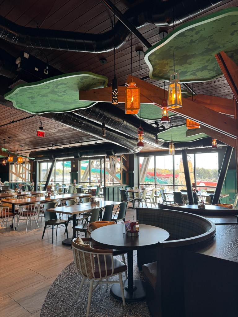 Interior view of a dining area at Great Wolf Lodge showcasing wooden beams, seating arrangements, unique ceiling decor, and large windows.