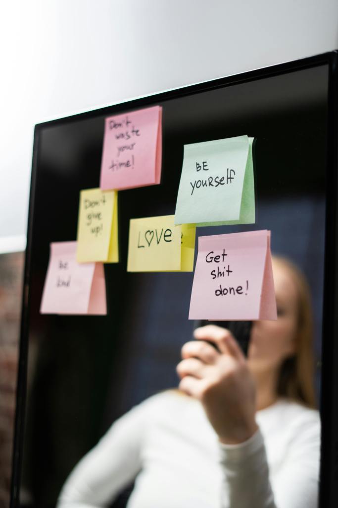 A mirror with multiple colorful sticky notes featuring motivational messages such as 'Don't waste your time!', 'BE yourself', 'LOVE', and 'Get shit done!'