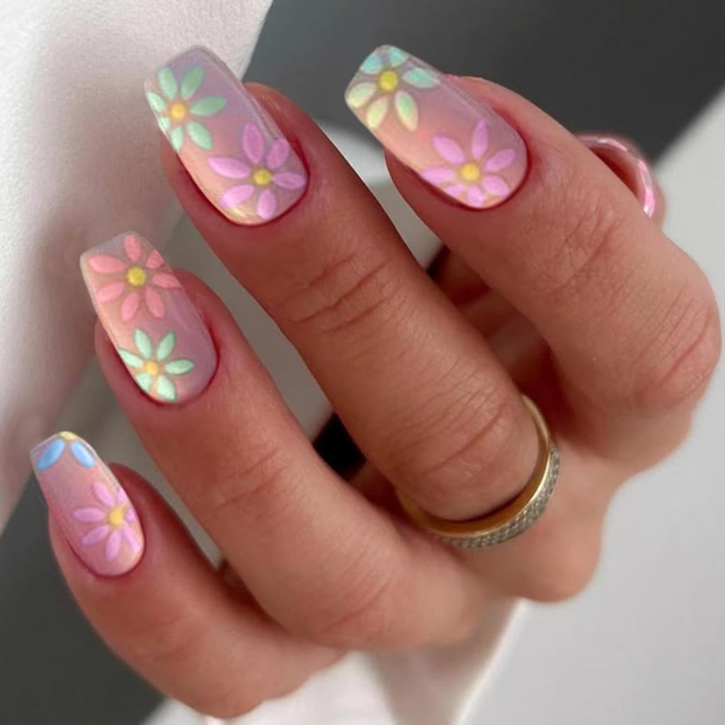 Close-up of a hand showing pink and pastel-colored floral nail art with a glossy finish, featuring gold and silver rings on the fingers.