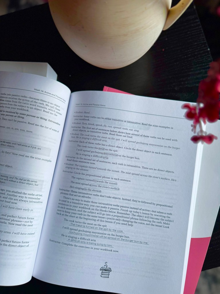 A close-up view of an open workbook page discussing active and passive voice, with text examples and instructional prompts. A ceramic pot and flower are visible in the background.
