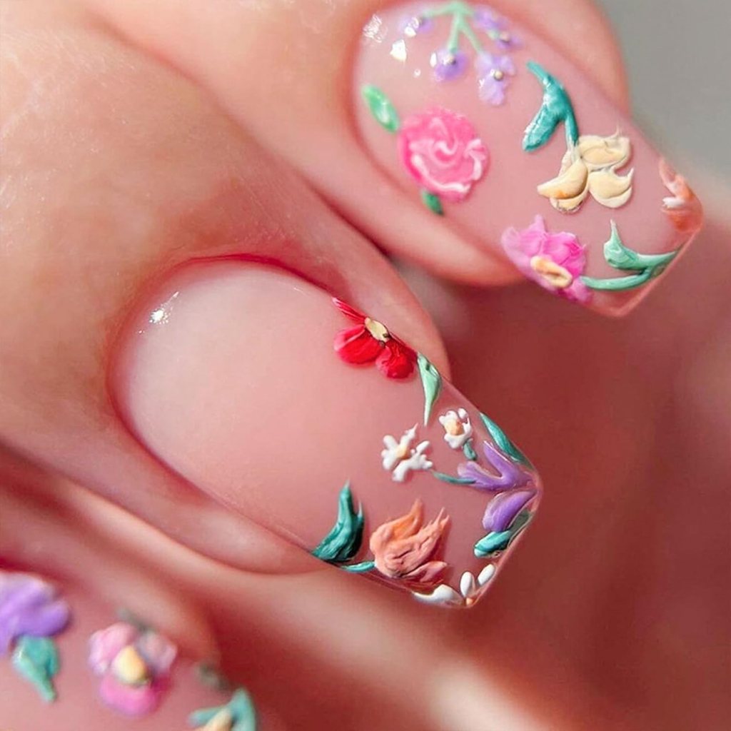 Close-up of manicured nails featuring intricate floral designs in various colors on a nude background.