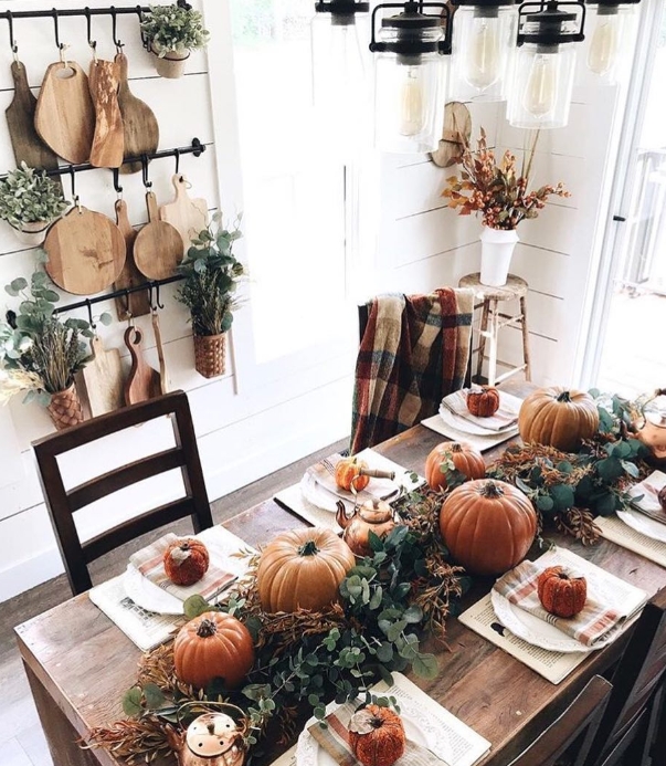 A beautifully styled Thanksgiving table featuring pumpkins, eucalyptus, and plaid accents, set in a cozy dining space with wooden decor and ambient lighting.