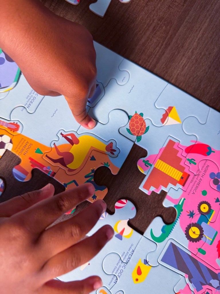 Child using both hands to place a piece into a world map puzzle featuring continents and animals.