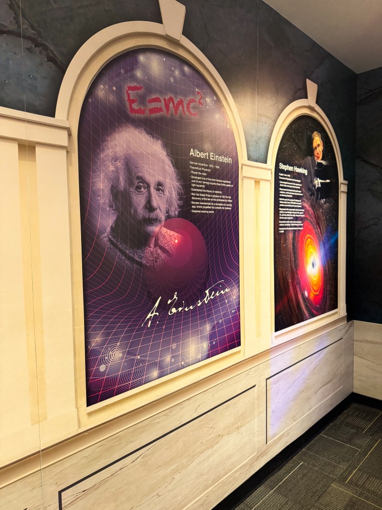 Exhibit displaying portraits of Albert Einstein and Stephen Hawking alongside descriptions of their contributions to science, featuring Einstein's equation E=mc².