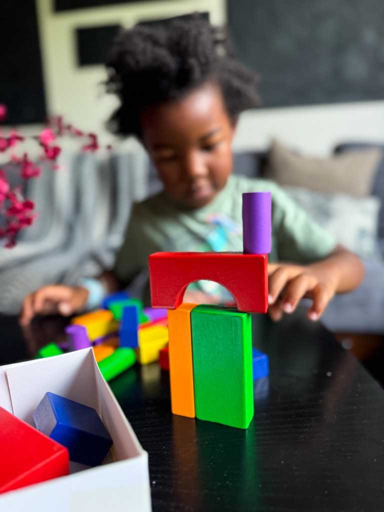 A child playing with colorful building blocks on a black table, focused on constructing a structure.