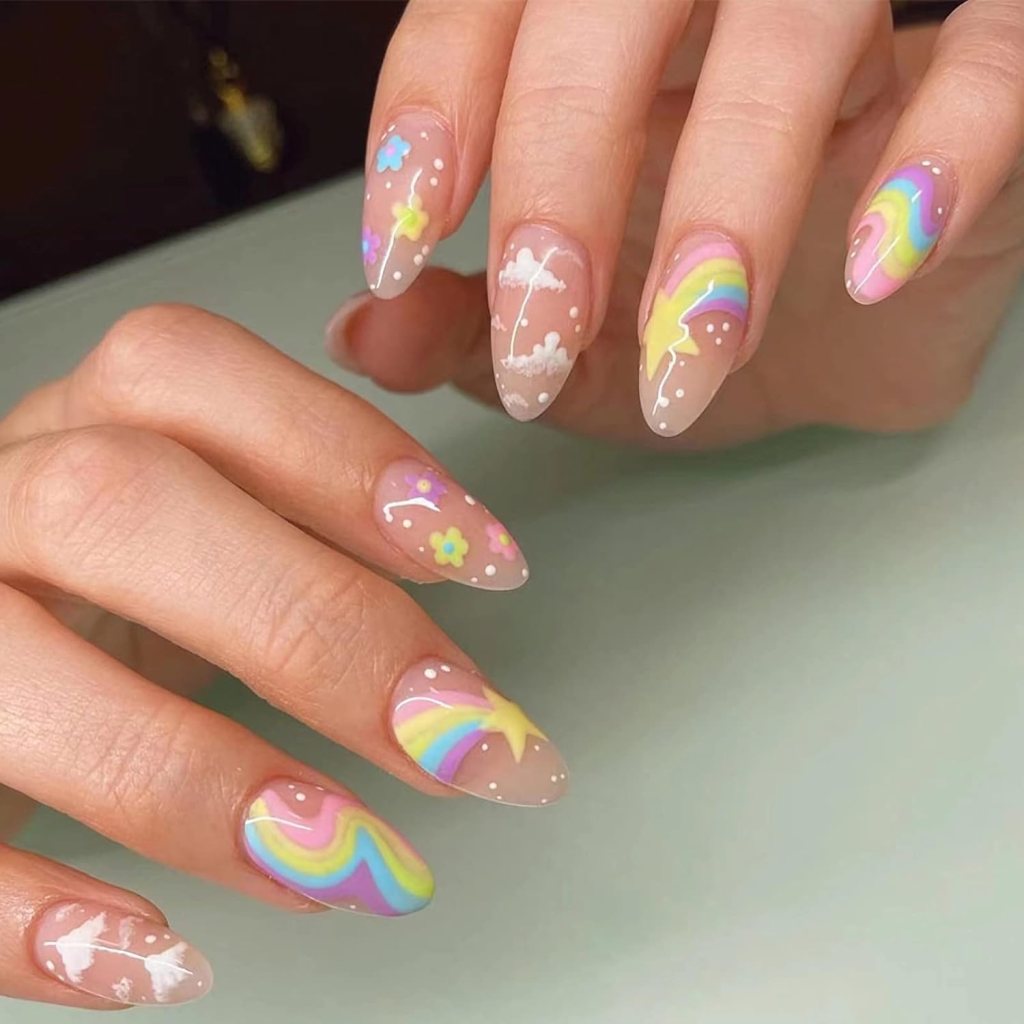 Close-up of a manicured hand featuring colorful nail art with designs including rainbows, stars, flowers, and clouds on a nude background.