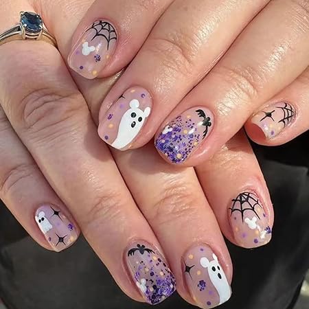 Short nails decorated with cute ghost faces, purple glitter, and spiderweb designs on a nude background, creating a playful Halloween-themed manicure.